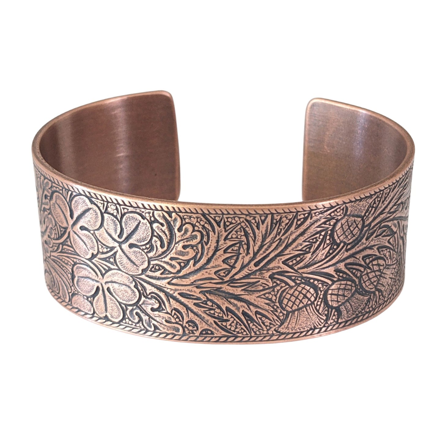 copper cuff bracelet with an embossed pattern of oak leaves, evergreen boughs, acorns, thistle, and clover. The impressed portions of the design are blackened.