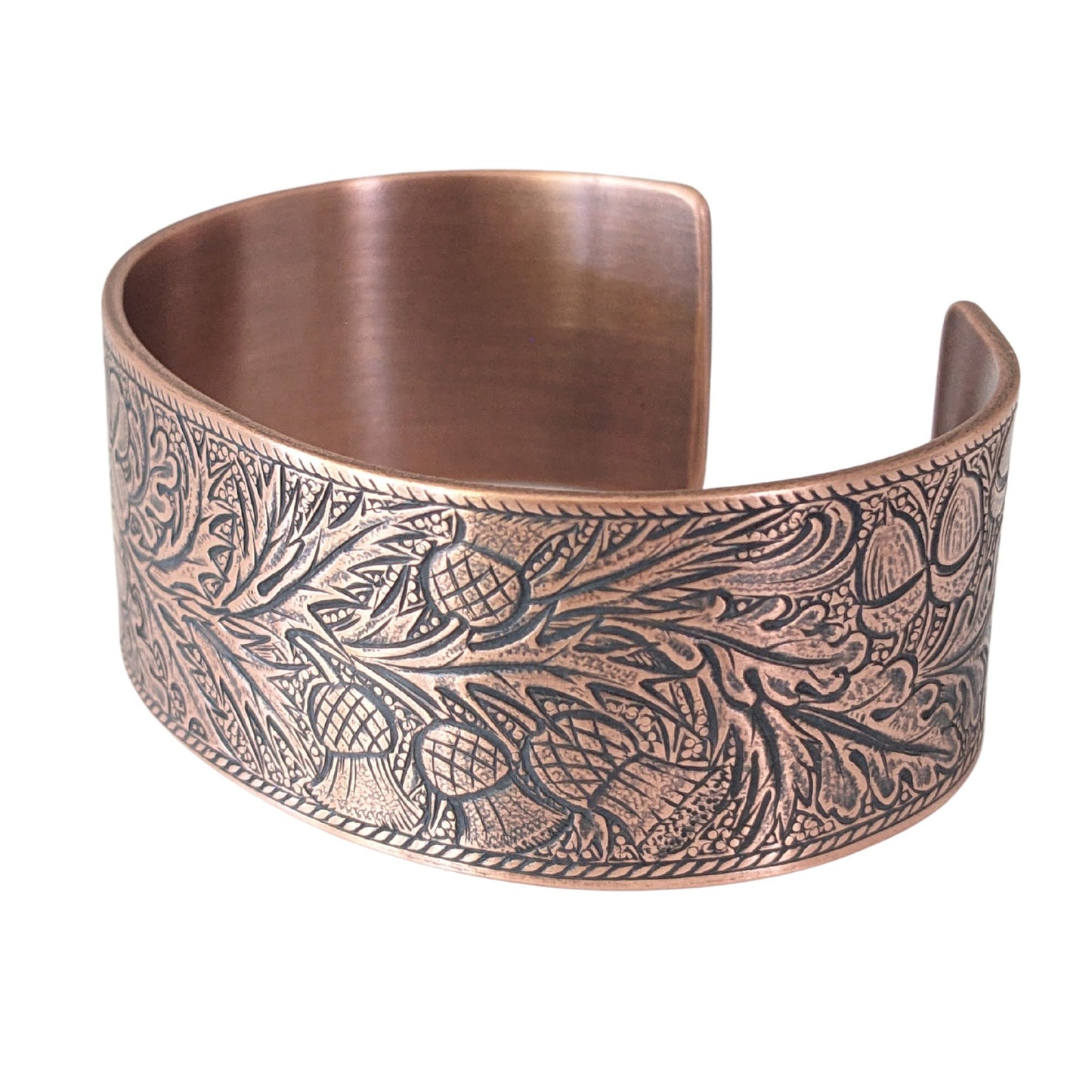 copper cuff bracelet with an embossed pattern of oak leaves, evergreen boughs, acorns, thistle, and clover. The impressed portions of the design are blackened.