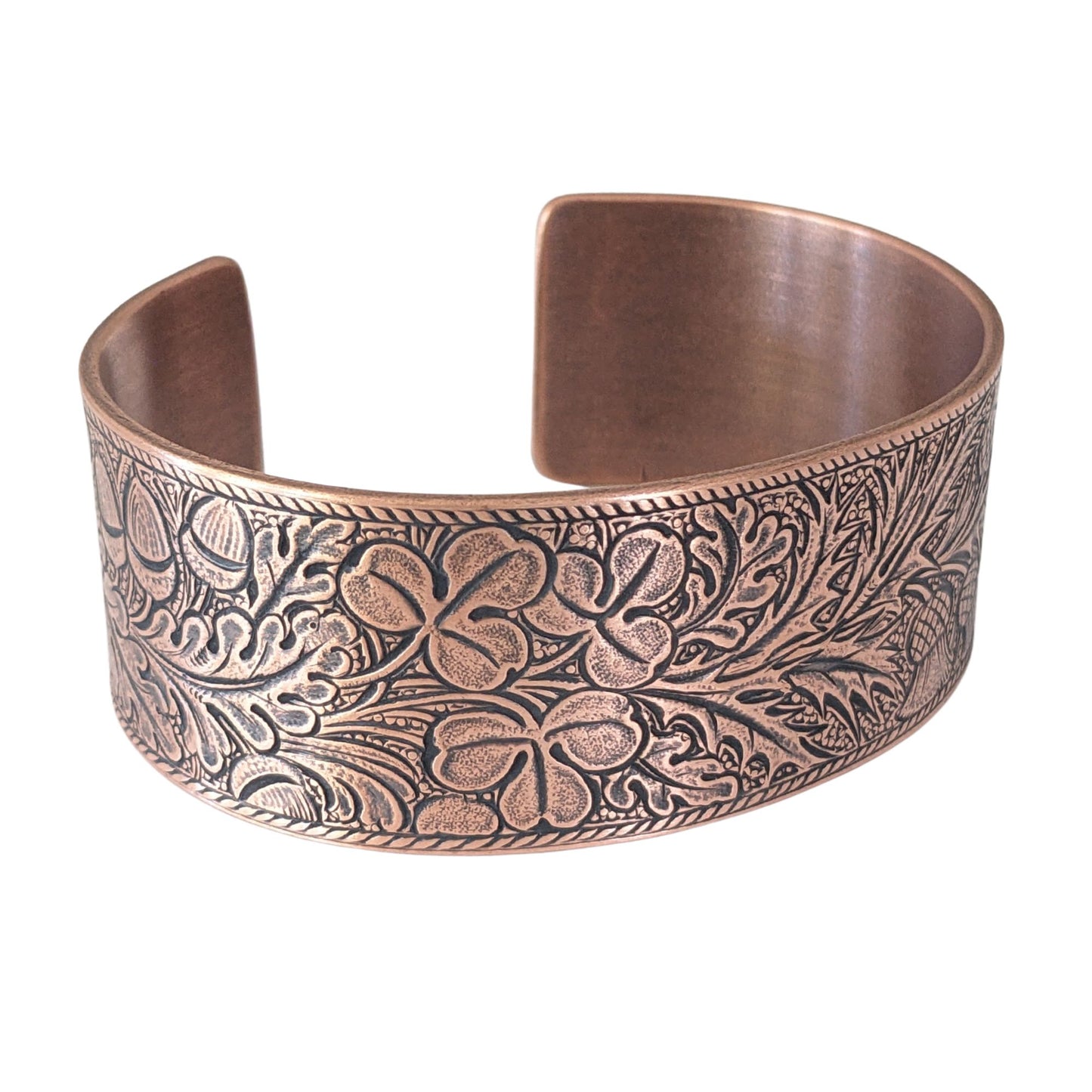 copper cuff bracelet with an embossed pattern of oak leaves, evergreen boughs, acorns, thistle, and clover. The impressed portions of the design are blackened.