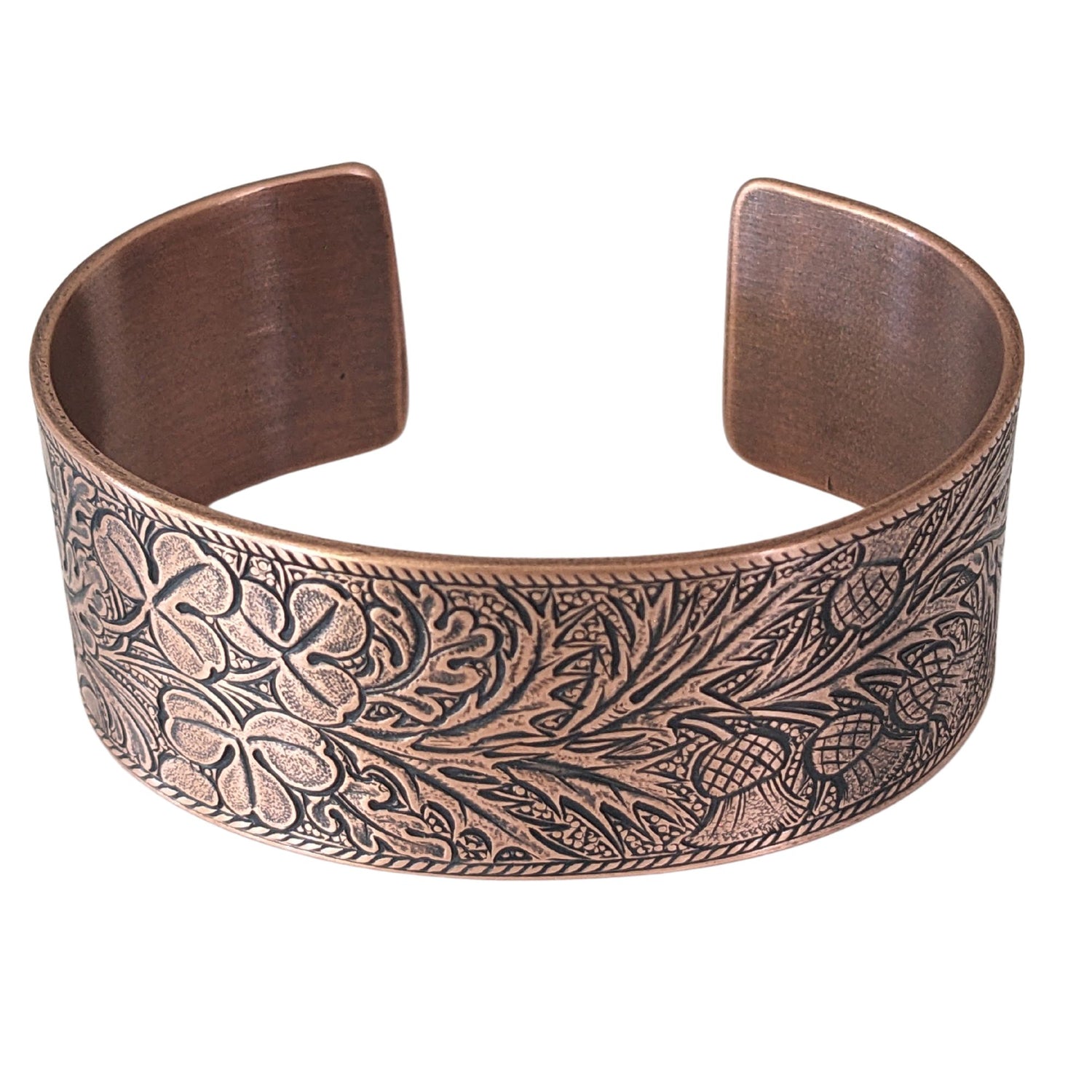 copper cuff bracelet with an embossed pattern of oak leaves, evergreen boughs, acorns, thistle, and clover. The impressed portions of the design are blackened.