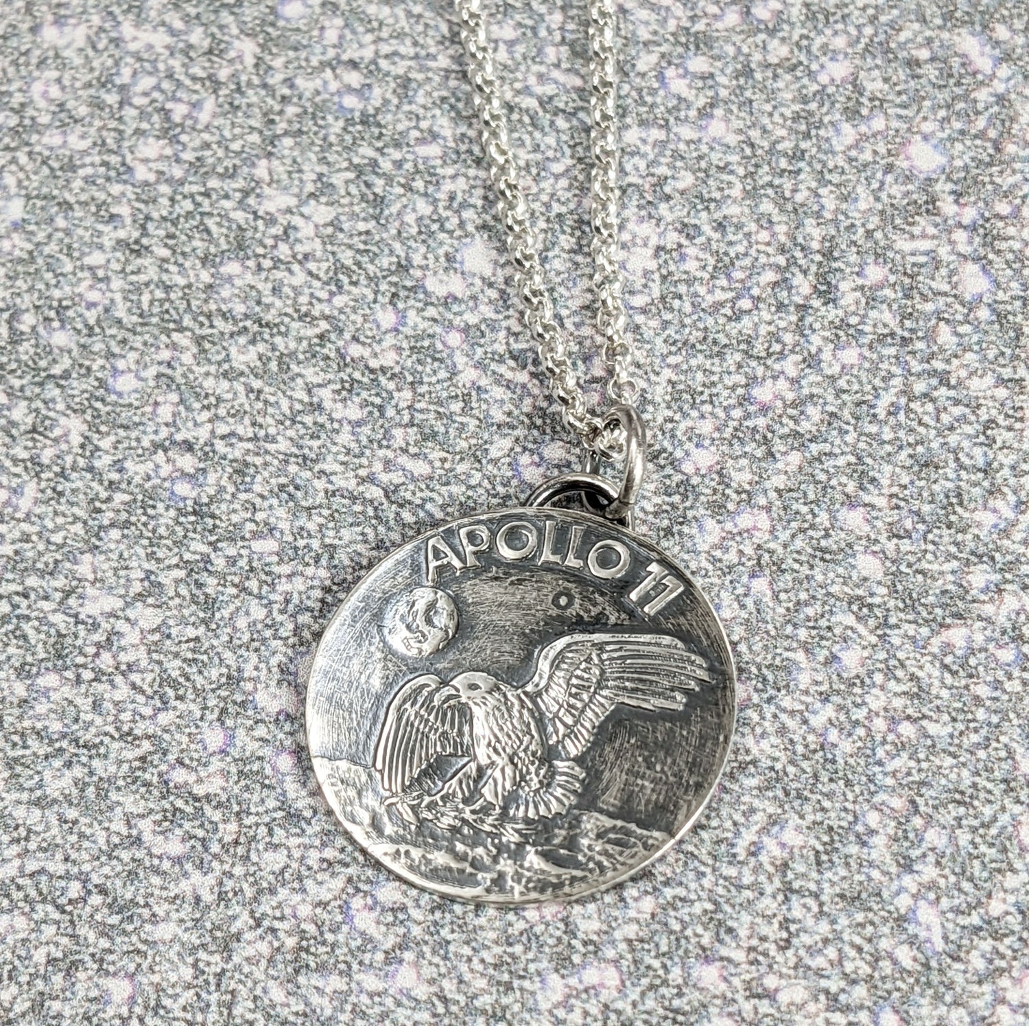 Handmade sterling silver pendant necklace signifying the landing of lunar module Eagle on the moon. The words Apollo 11 are in the background above the earth, and an eagle is approaching the moon surface.