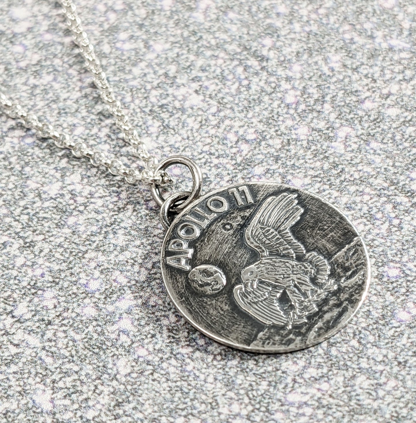 Handmade sterling silver pendant necklace signifying the landing of lunar module Eagle on the moon. The words Apollo 11 are in the background above the earth, and an eagle is approaching the moon surface.