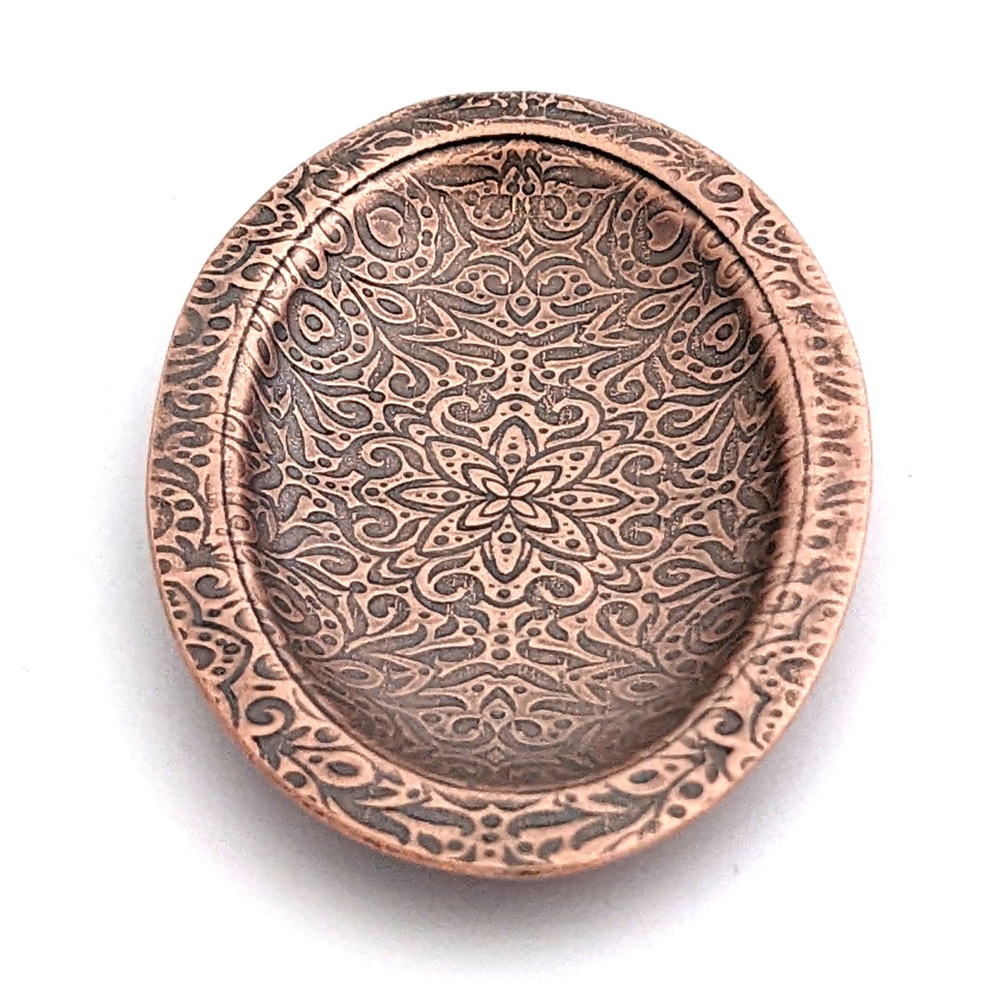 Copper oval ring dish with abstract garden flowers and leaves design.  Dish is 2 inches by three inches with a raised lip.