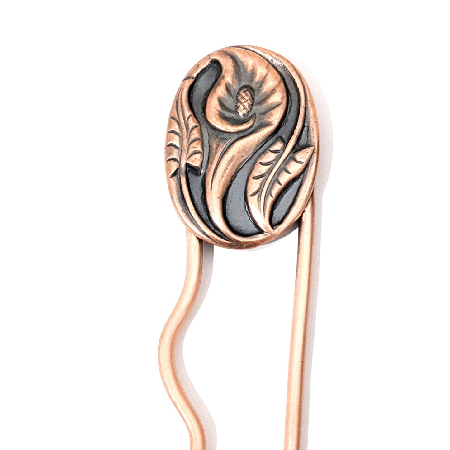 Copper hair fork with a calla lily flower design. Large oval copper piece with a single calla flower in the middle. A stem and leaf facing upward on the left side of the oval, and one facing downward on the right side of the oval. 