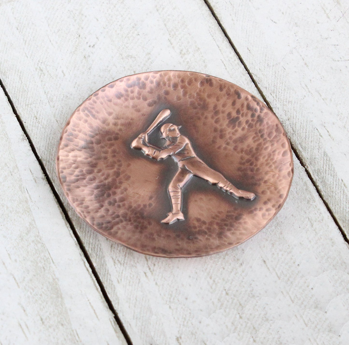 Small copper ring or trinket dish with raised impression of an old time baceball player at bat. The dish edges have a hsammered dappled texture and the edges are slightly curved up to form a shallow bowl.
