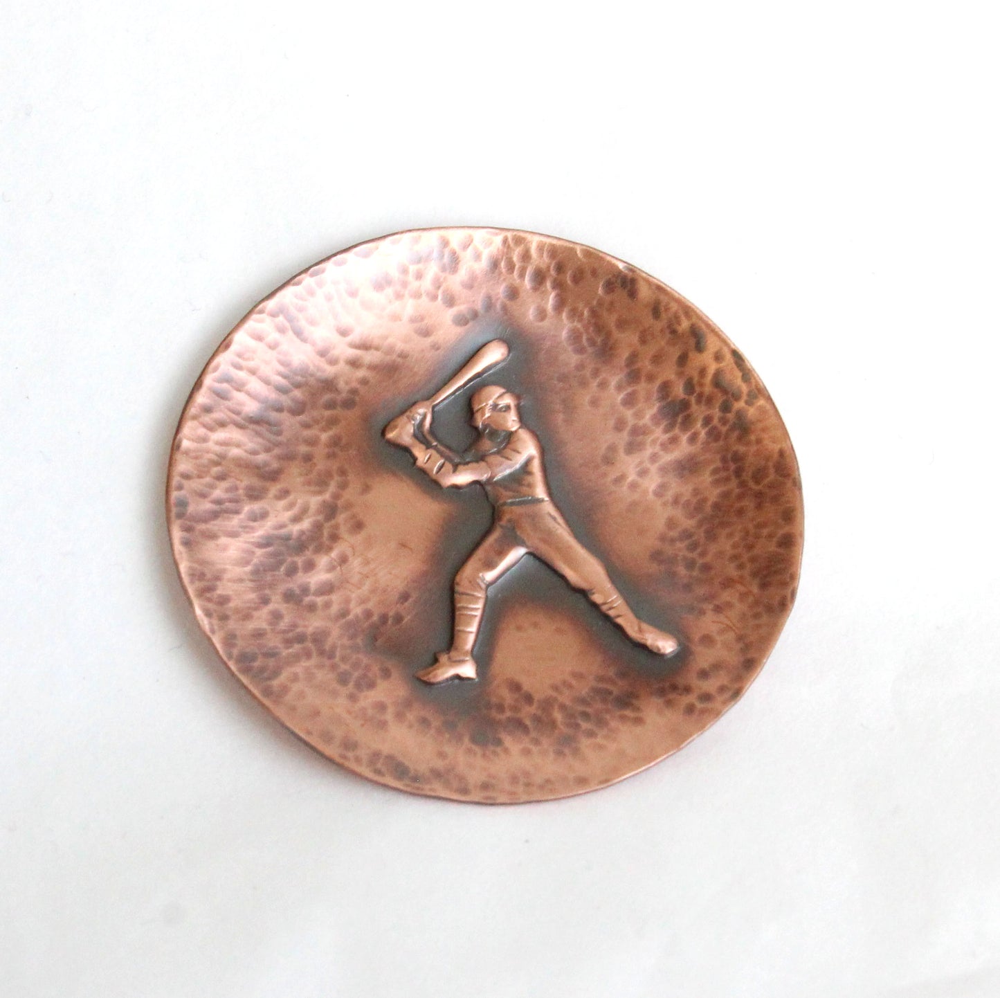 Small copper ring or trinket dish with raised impression of an old time baceball player at bat. The dish edges have a hsammered dappled texture and the edges are slightly curved up to form a shallow bowl.