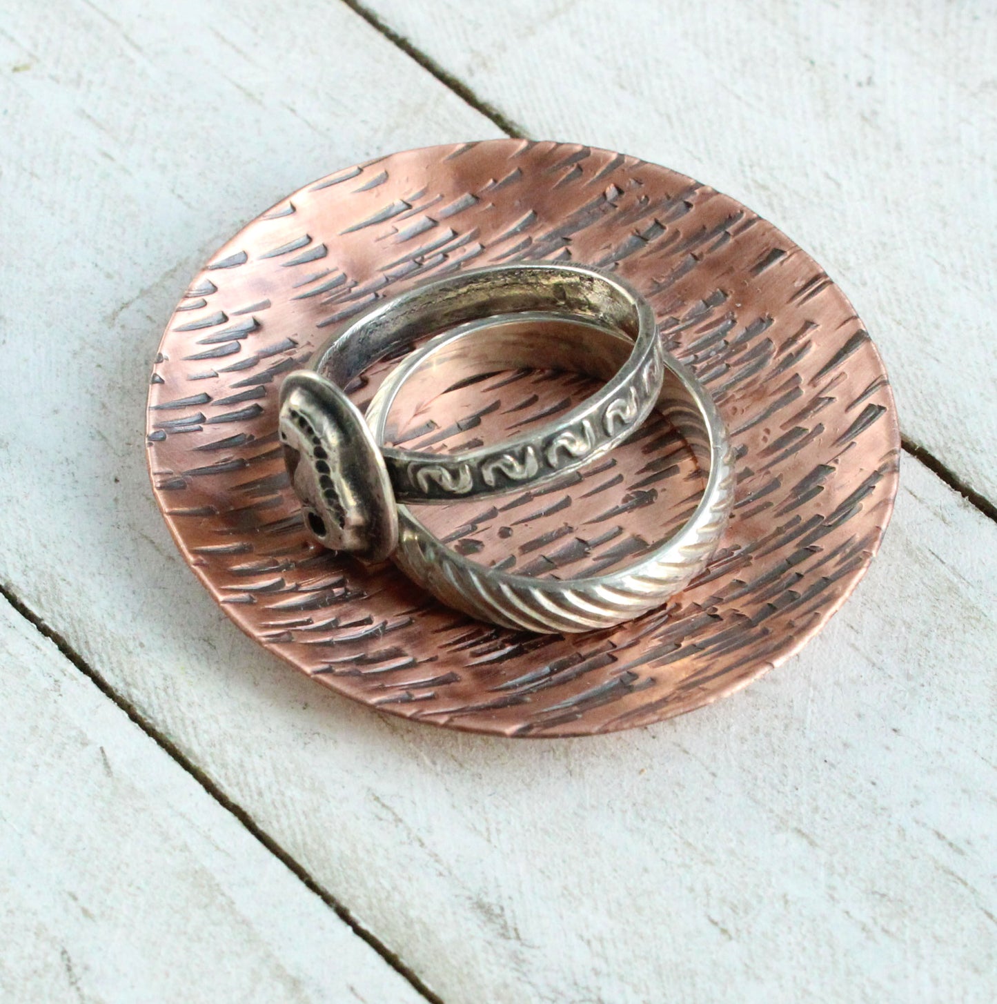 Small copper ring jewelry or trinket dish with a hammered texture resembling birch bark. The edges are curved up to form a shallow bowl.