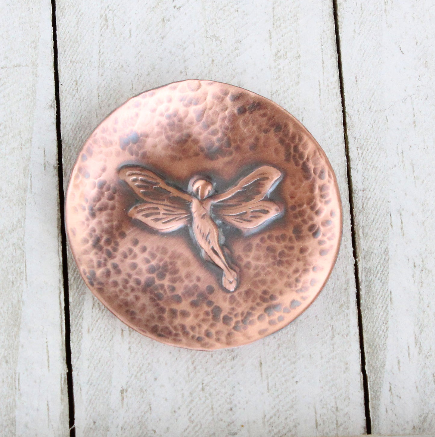 Small copper copper dish for rings, jewelry, trinkets. In middle there is a raised image of a fairy in flight. The background is dappled hammer texture, the sides are raised to form a shallow bowl.