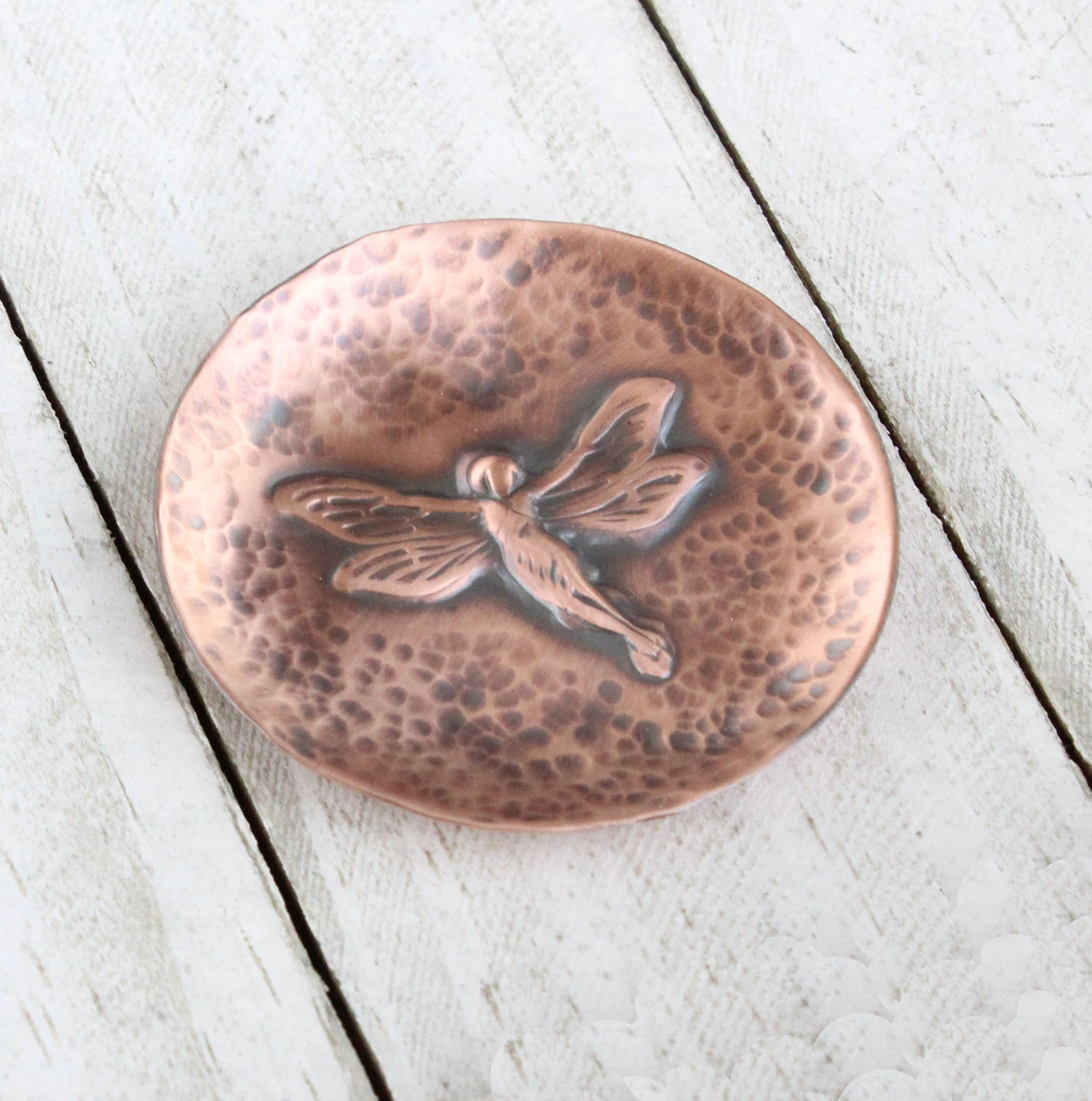 Small copper copper dish for rings, jewelry, trinkets. In middle there is a raised image of a fairy in flight. The background is dappled hammer texture, the sides are raised to form a shallow bowl.