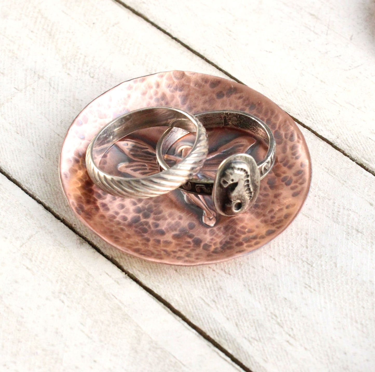 Small copper copper dish for rings, jewelry, trinkets. In middle there is a raised image of a fairy in flight. The background is dappled hammer texture, the sides are raised to form a shallow bowl.