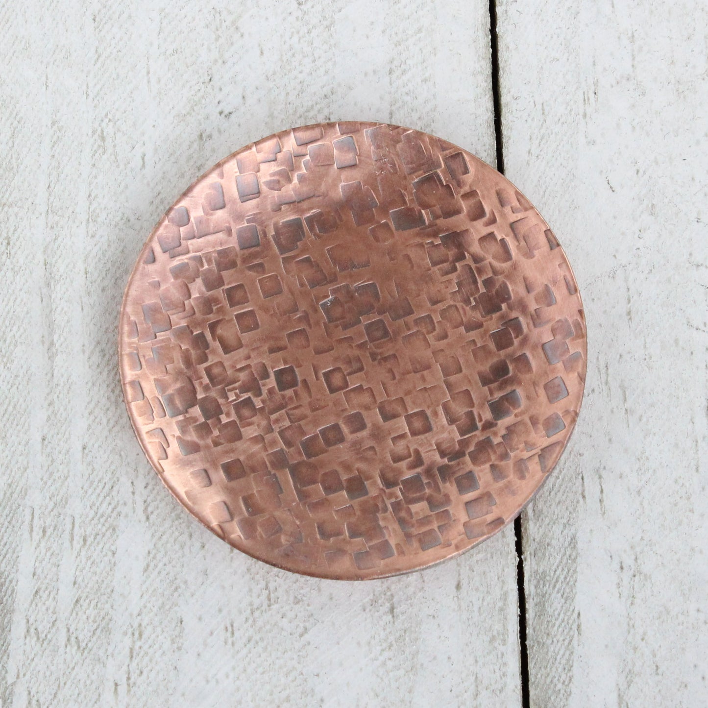 Small copper ring dish for rings, jewelry, and trinkets. Hammered texture pattern, the pattern is random small squares. Slightly raised edges form a shallow bowl.