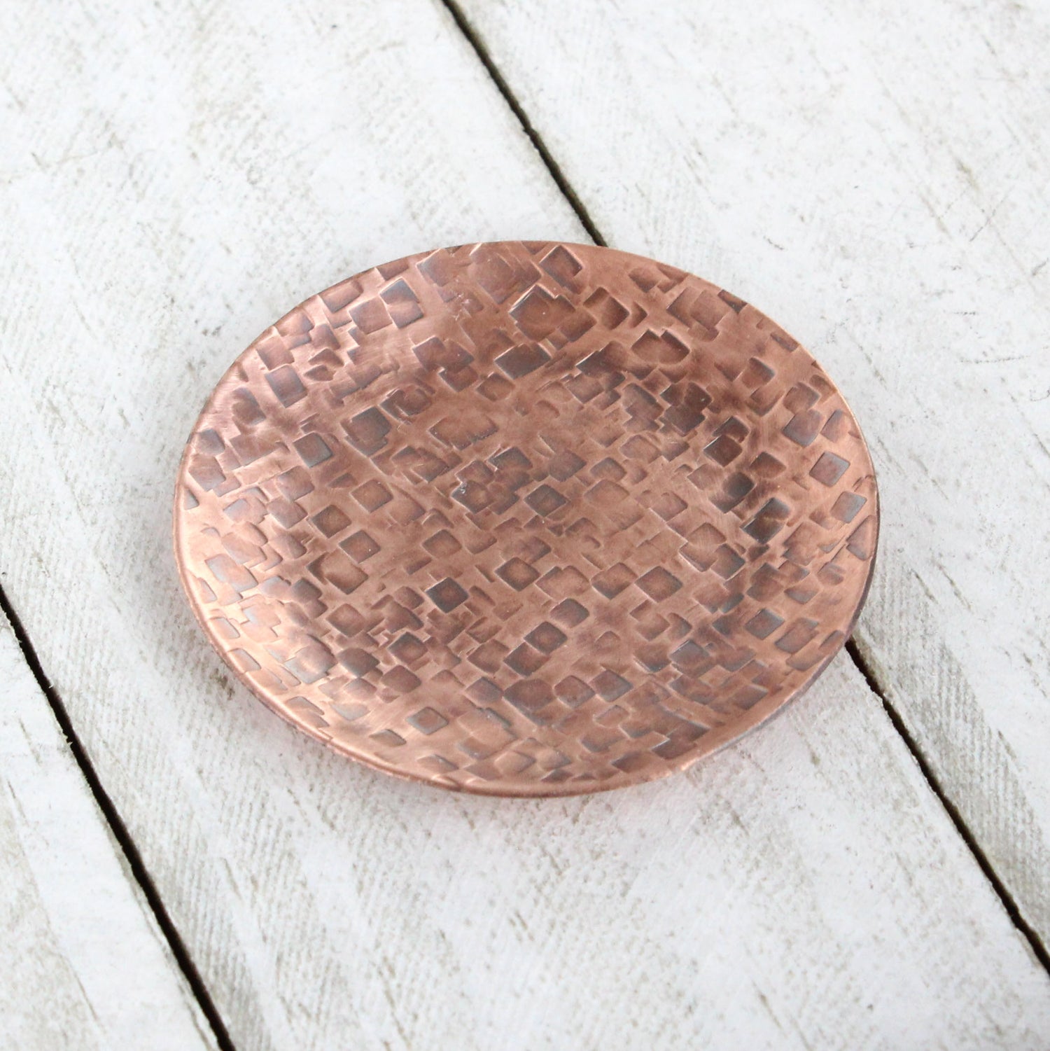 Small copper ring dish for rings, jewelry, and trinkets. Hammered texture pattern, the pattern is random small squares. Slightly raised edges form a shallow bowl.