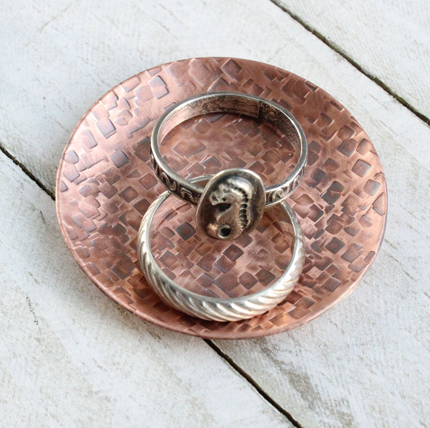 Small copper ring dish for rings, jewelry, and trinkets. Hammered texture pattern, the pattern is random small squares. Slightly raised edges form a shallow bowl.