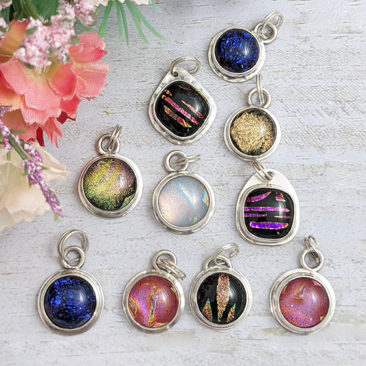 Jewelry charms. Dichroic glass round and square shapes in different colors set in sterling silver with split rings added to hang from bracelet or necklace