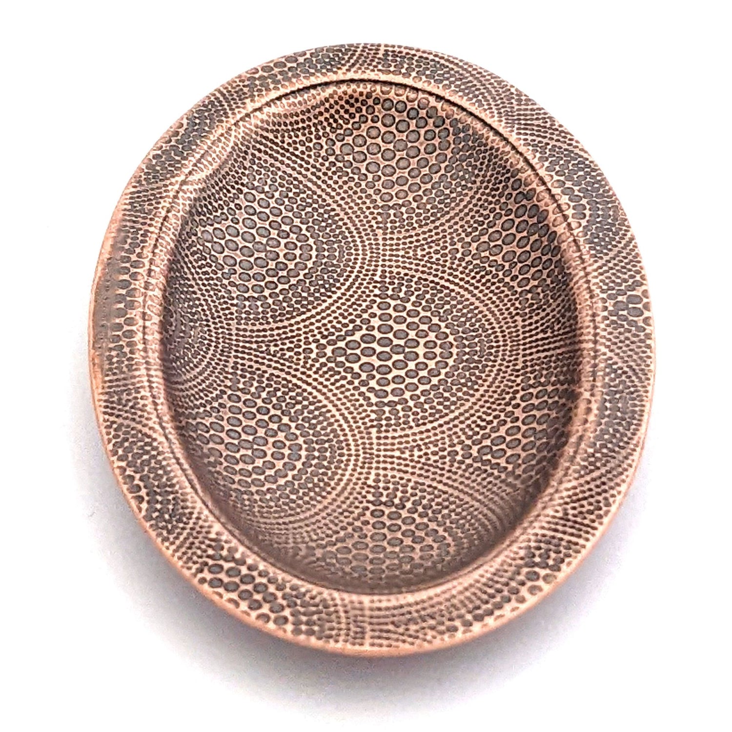 Copper oval ring dish with repeating pattern of dotted arches.  Dish is 2 inches by three inches with a raised lip.