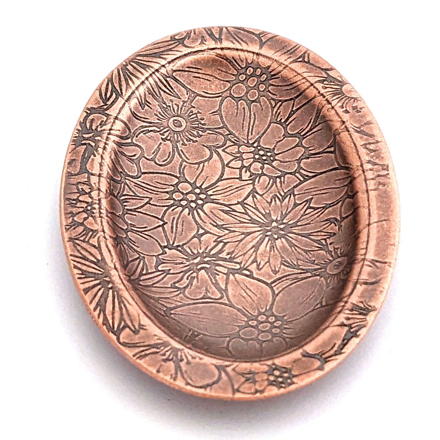 Copper oval ring dish with repeating pattern of assortment of flowers.  Dish is 2 inches by three inches with a raised lip.