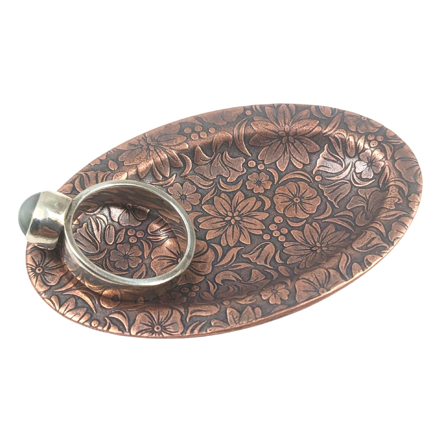 Oval copper ring dish with raised edge. Design of a variety of garden flowers, leaves, and berries covers the entire surface. Stages with a ring.