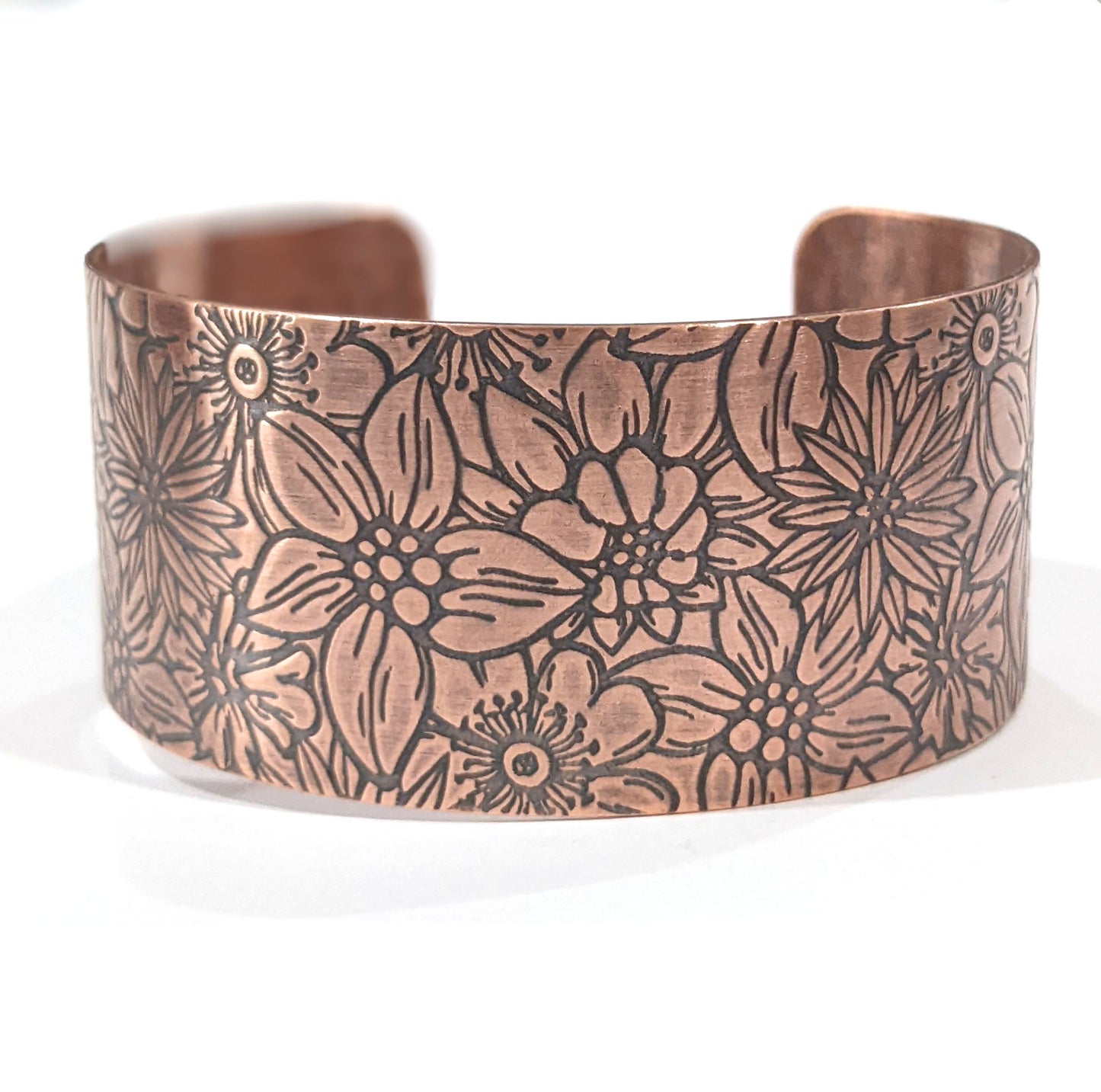 Wide copper bracelet with impressed design of flowers. The entire cuff is covered in various kinds of flowers in full bloom.