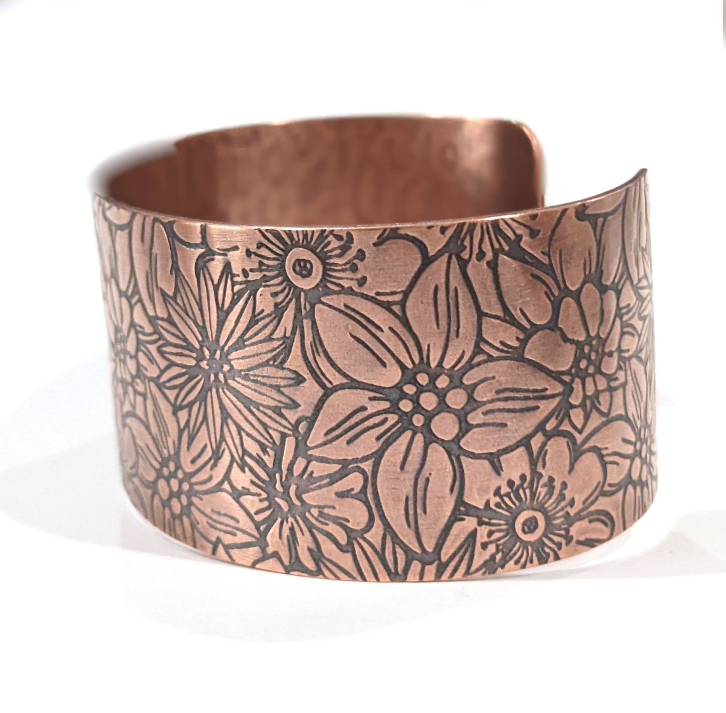 Wide copper bracelet with impressed design of flowers. The entire cuff is covered in various kinds of flowers in full bloom. Side View