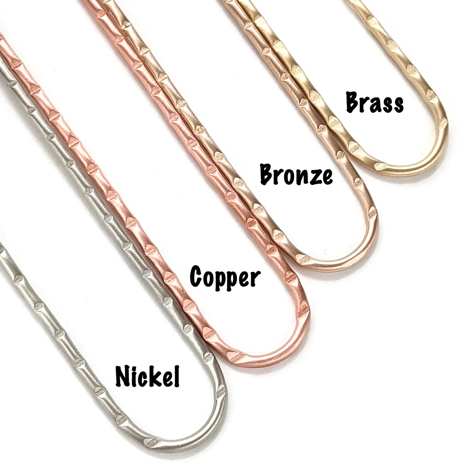Metal hair forks shown in the four options - nickel, copper, bronze, and brass. This picture shows the detailed deep line grooves in the top portion of each hair stick. The names of the metals are also shown. Hair sticks are an easy alternative to cheap butterfly hair clips for long hairstyles.