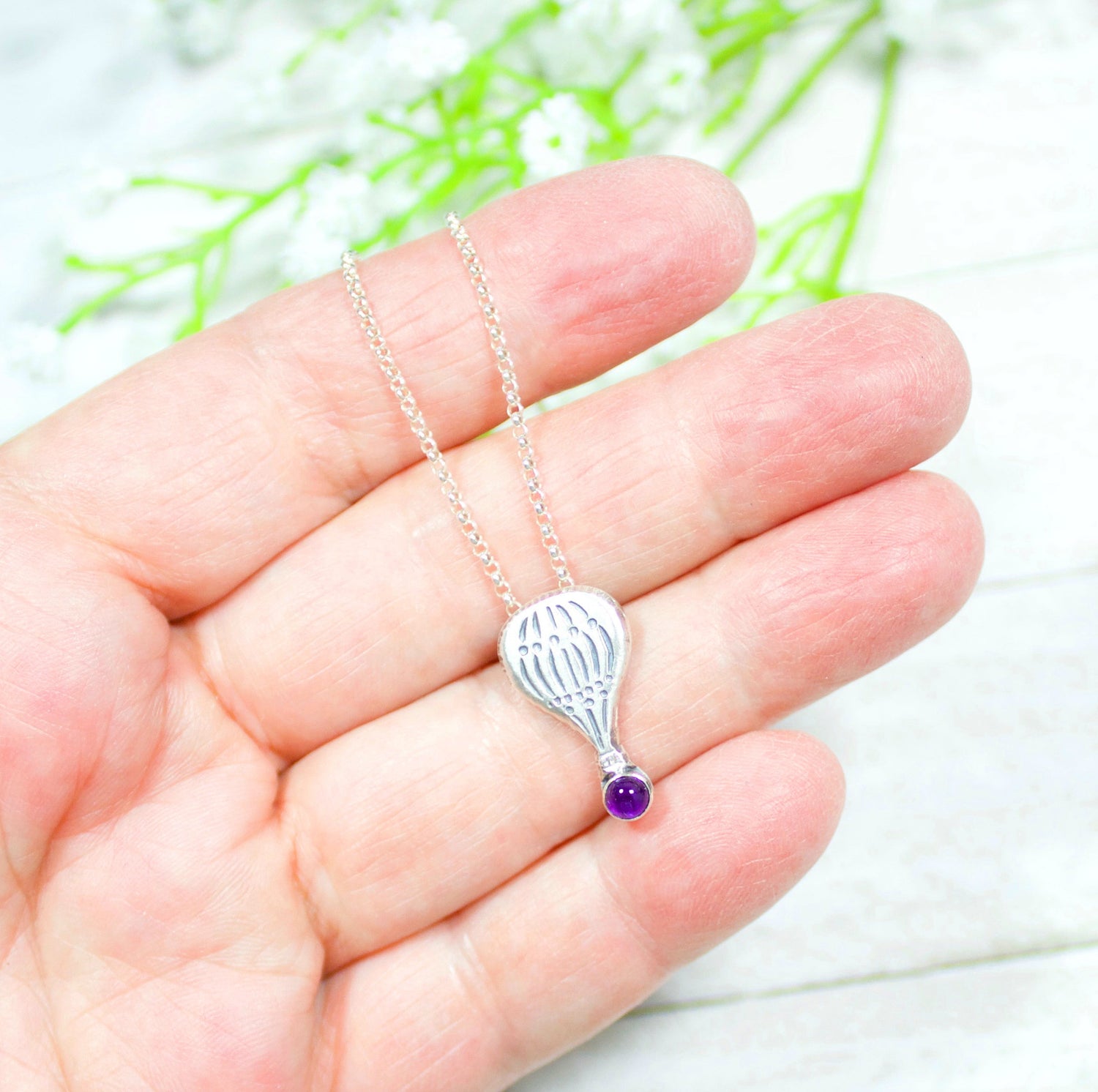 Hot air balloon shaped sterling silver pendant with a gemstone cabochon placed where the basket would be.  Shown with an amethyst and being held in the hand of a model to show size.