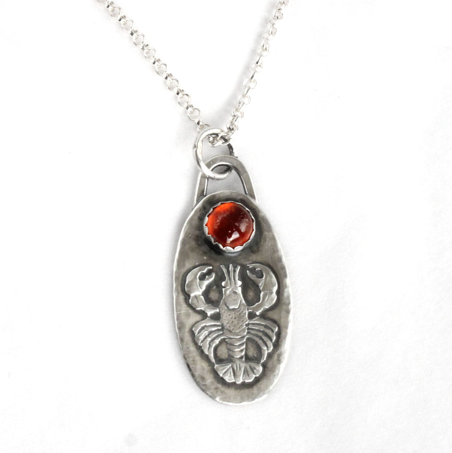 Lobster Sterling Silver Pendant with Hessonite Garnet. The pendand has a detailed raised impression of a lobster. Above the lobster is a 6mm hessonite garnet stone. The pendant is 1-1/4 inches long and about 5/8 inches wide and comes on an 18 inch sterling silver rolo chain.