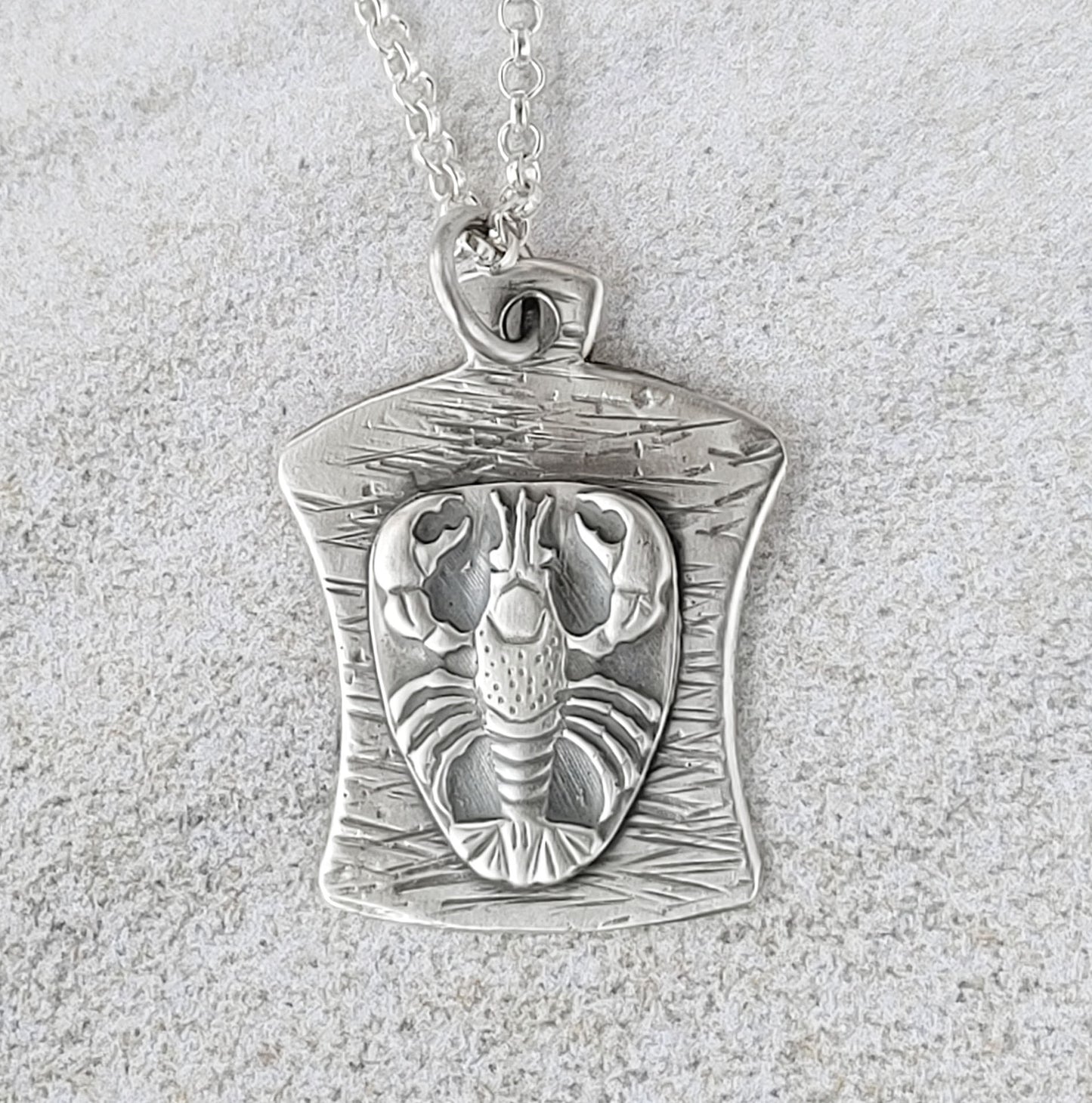 This pendant is a finely detailed raised lobster impression, the curved background has a hammered line texture.  This pendant is 1 inch long and about 3/4 inches across at the widest point. It comes on an 18 inch sterling silver chain.