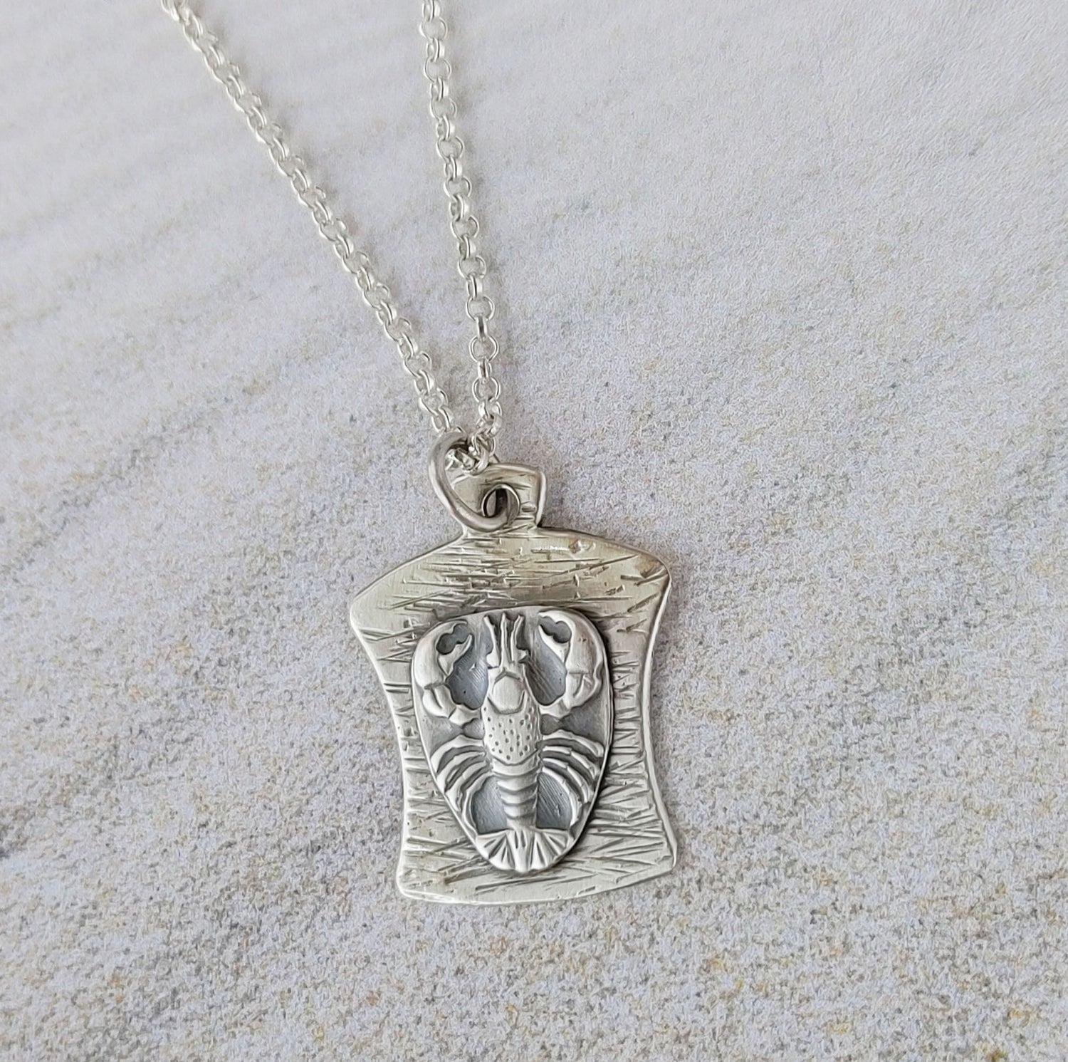 This pendant is a finely detailed raised lobster impression, the curved background has a hammered line texture.  This pendant is 1 inch long and about 3/4 inches across at the widest point. It comes on an 18 inch sterling silver chain.