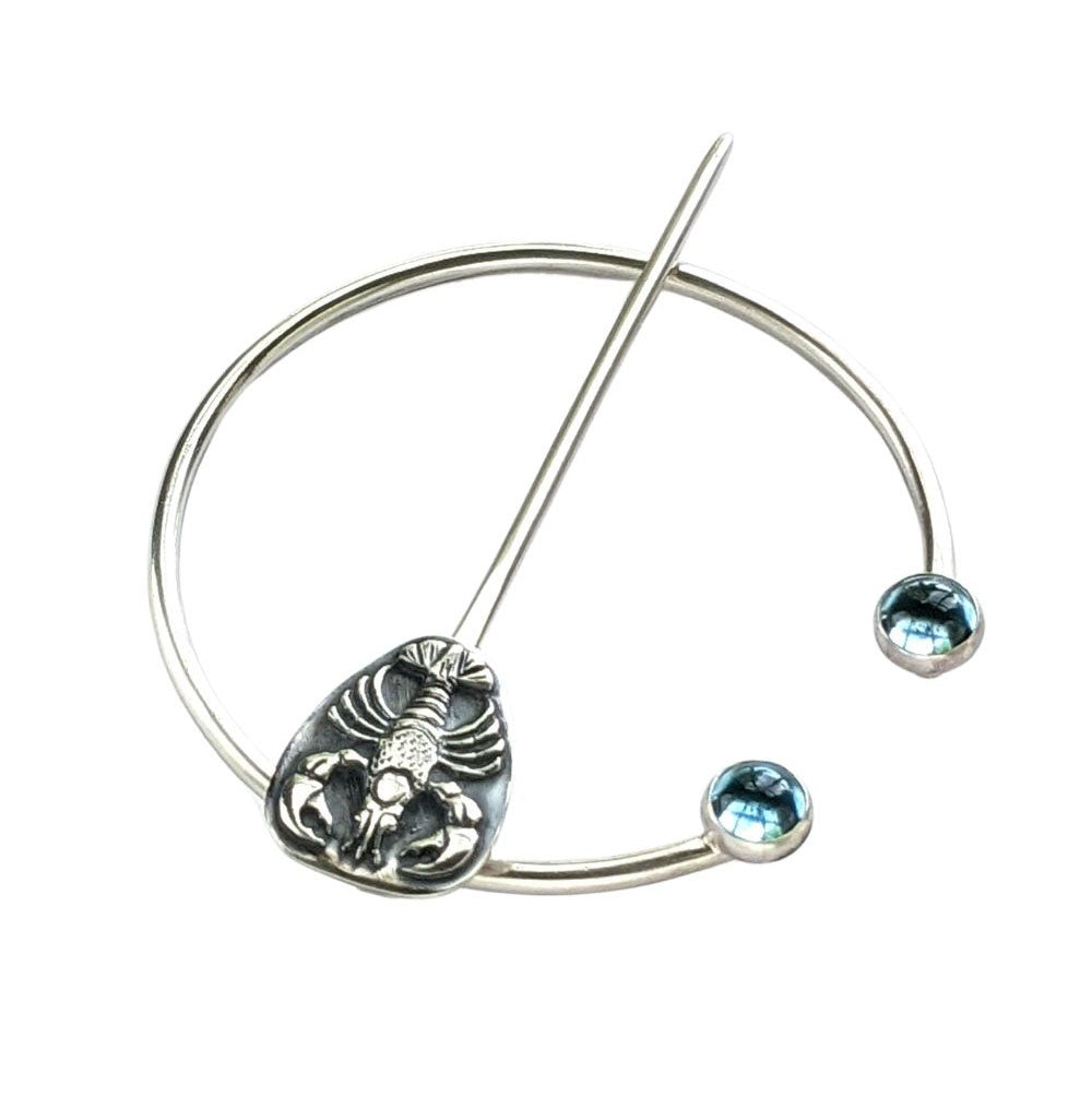 Sterling silver penannular brooch. The tip of the stem is decorated with a detailed dimensional lobster, and the ends of the loop have bright swiss blue topaz gemstone cabochons.