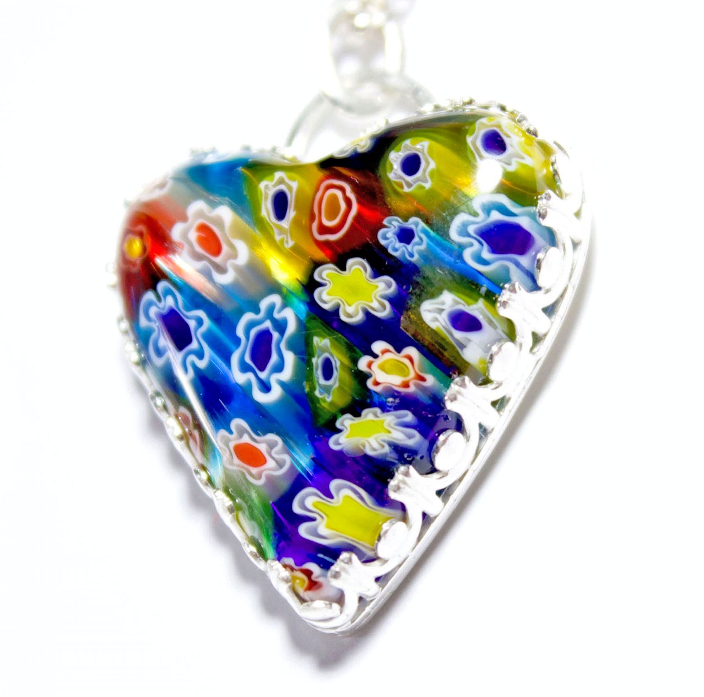 Heart shaped pendant made of millifiore glass. The heart is clear glass filled with glass tubes that are shaped like flowers and go from the front to the back of the heart. Multi color includes red, blue, yellow, and white. Surrounded by a heavy detailed gallery wire.