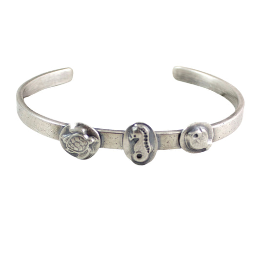 Sterling silver cuff bracelet with sea creatures. The cuff is 5mm x 2mm, so is slim, and is textured to resemble sand. There are three solid sterling silver ovals attached, one of a turtle, one of a seahorse, and one of a fish.