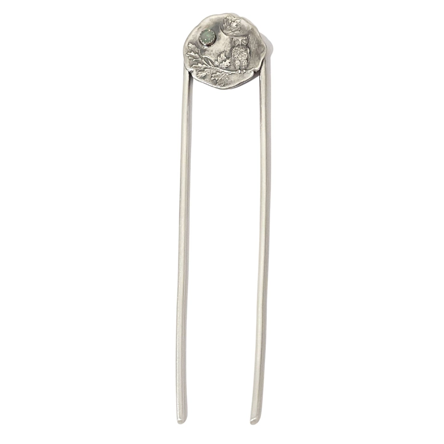 Sterling silver hair fork. The design at the top of the hair fork is a round sterling silver piece with a 3 dimensional design of an owl sitting on a tree branch. The branch has leaves, oak perhaps. Above the leaves there is a white opal gemstone to represent the moon.  This picture shows both the design at the top and the forks, which are straight and made of sterling silver.