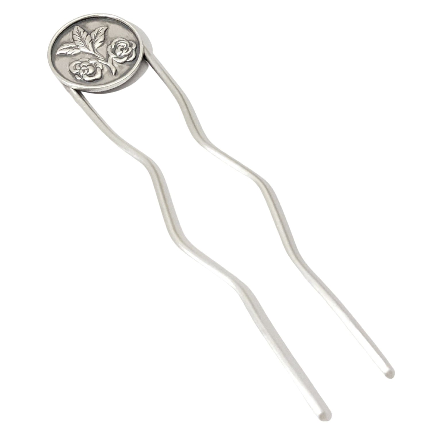 Sterling silver hair fork. Attached to top of fork is a round piece of silver with a rounded border edge. The sheet has a raised design of two roses growing off of a branch clipping and at the end of the branch there are three leaves.