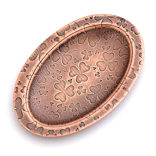 Copper oval ring dish with repeating pattern of shamrocks.  Dish is 2 inches by three inches with a raised lip.