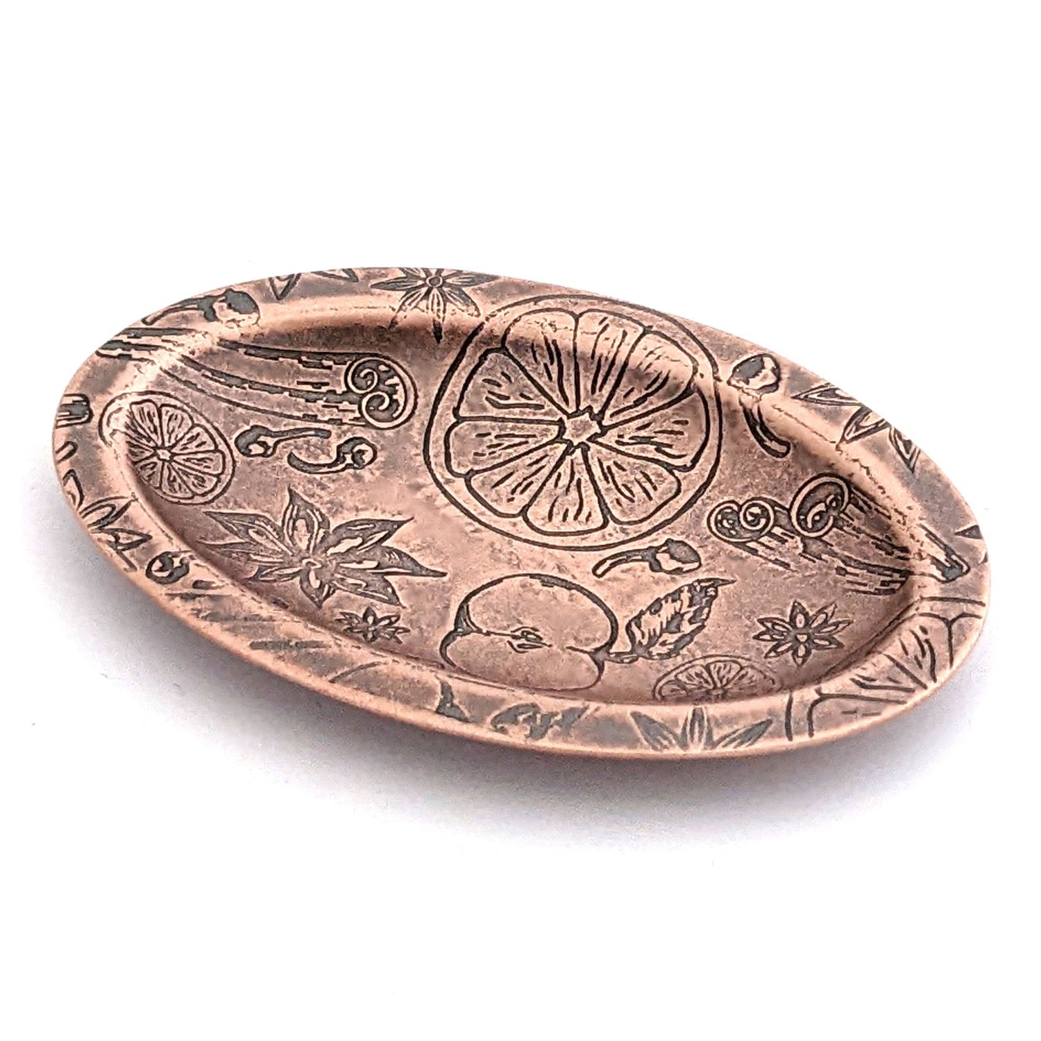 Copper oval ring dish with design of ingredients used in winter spice drinks, including apples oranges nutmeg cinnamon and clove.  Dish is 2 inches by three inches with a raised lip.