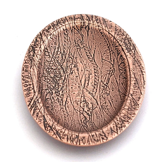 Copper oval ring dish with design of waves in a stormy sea. Dish is 2 inches by three inches with a raised lip.