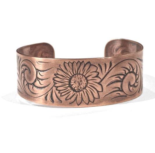 Copper cuff bracelet with a sunflower in the middle , surrounded by abstract flourish swirls.