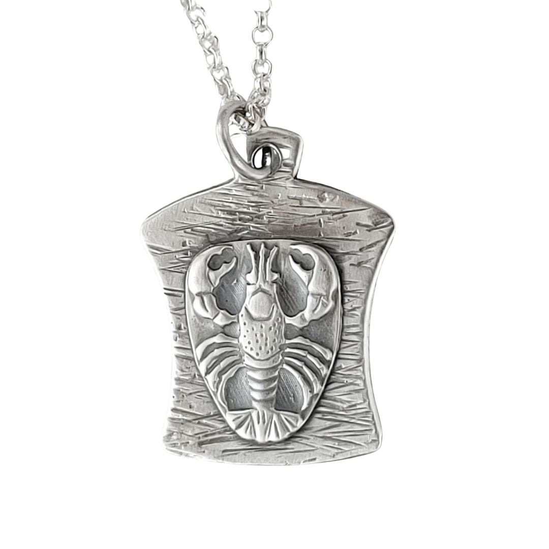 This pendant is a finely detailed raised lobster impression, the curved background has a hammered line texture.  This pendant is 1 inch long and about 3/4 inches across at the widest point. It comes on an 18 inch sterling silver chain.