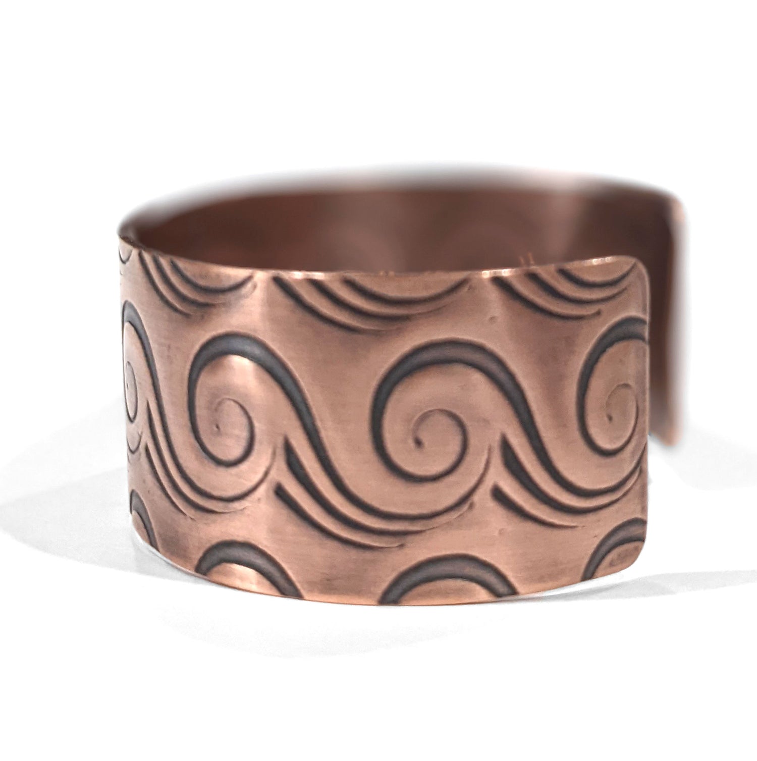 Copper cuff bracelet with a series of abstract line waves that wrap the entire cuff. Meant to resemble an ocean wave. Side view.