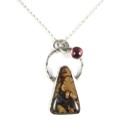 Stefoinite and Rhodolite Garnet pendant. The main stone is a tall triangle, brown and black. The black design looks like a leafless tree on a hilltop. The garnet represents a blood moon, which is what they call a lunar eclipse.