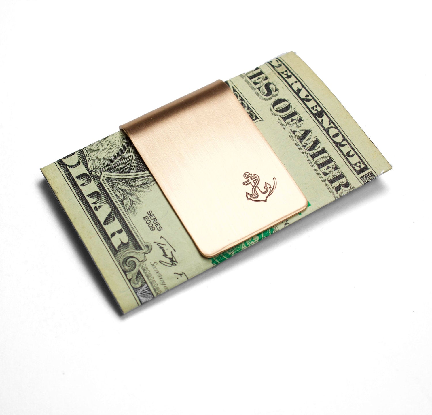 Anchor and Rope Money Clip. A small money clip with a stamped image of a boat anchor wrapped in a length of rope. The stamped design is darkened (oxidized). The money clip is shown in bronze metal and is shown actual size with a US dollar bill.