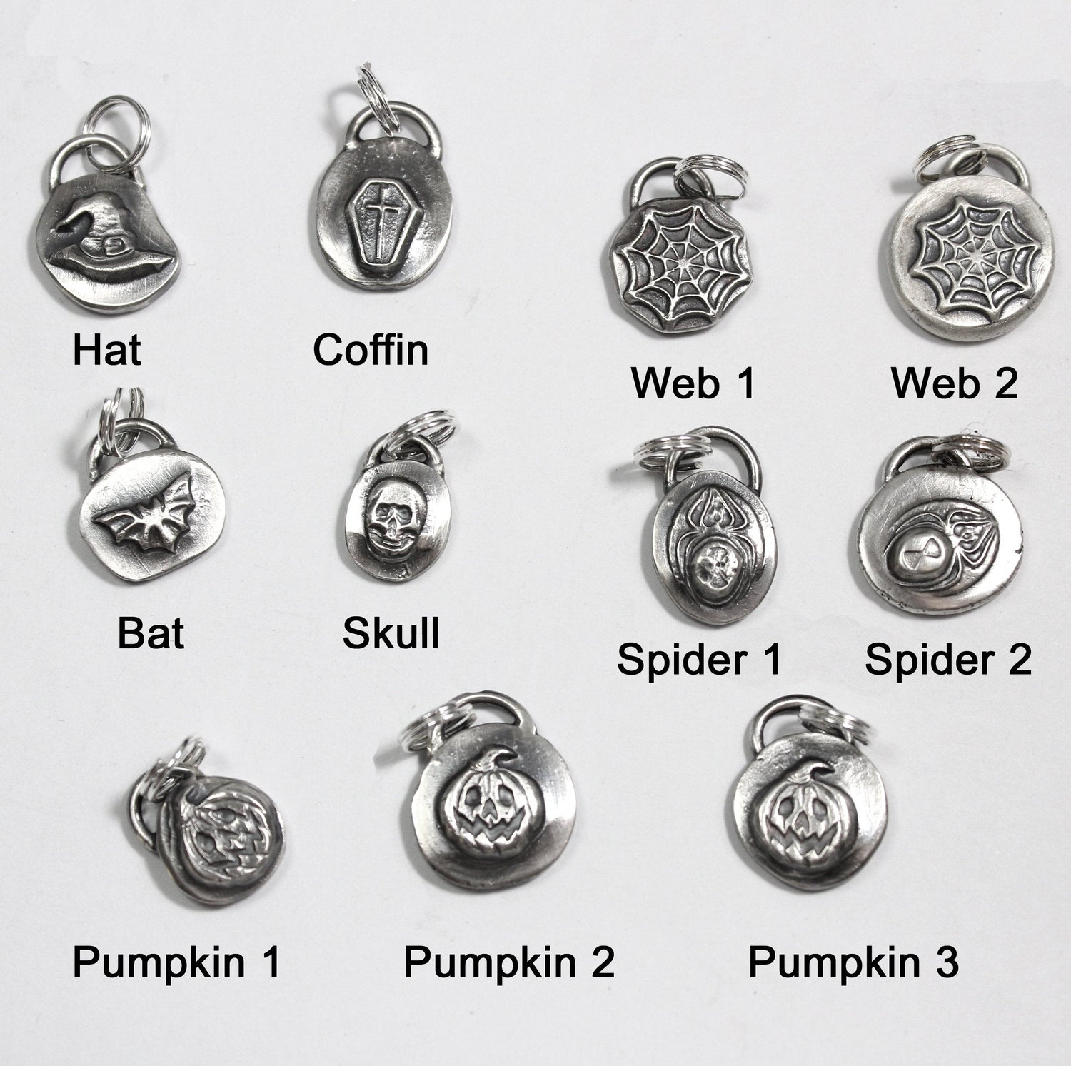 Halloween or Goth inspired sterling silver charms. Each charm is around one half inch, give or take. There's a loop at the top with a sterling silver split ring. The designs are bat, witch hat, coffin with cross, spider web, skull, black widow spider, and jack o lantern. Shown with names of each design.