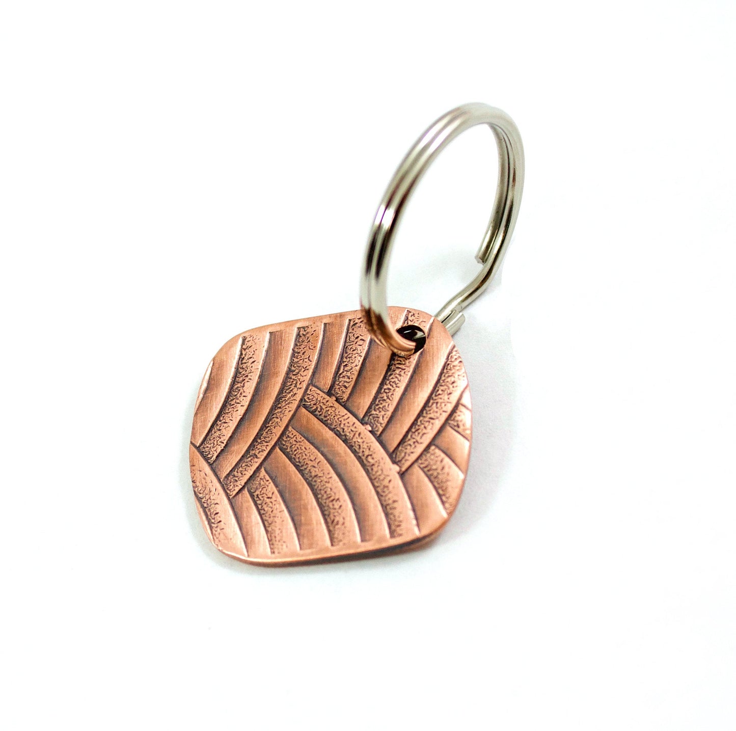 Copper keychain with a textured pattern of overlapping arches. Square with softly rounded corners.