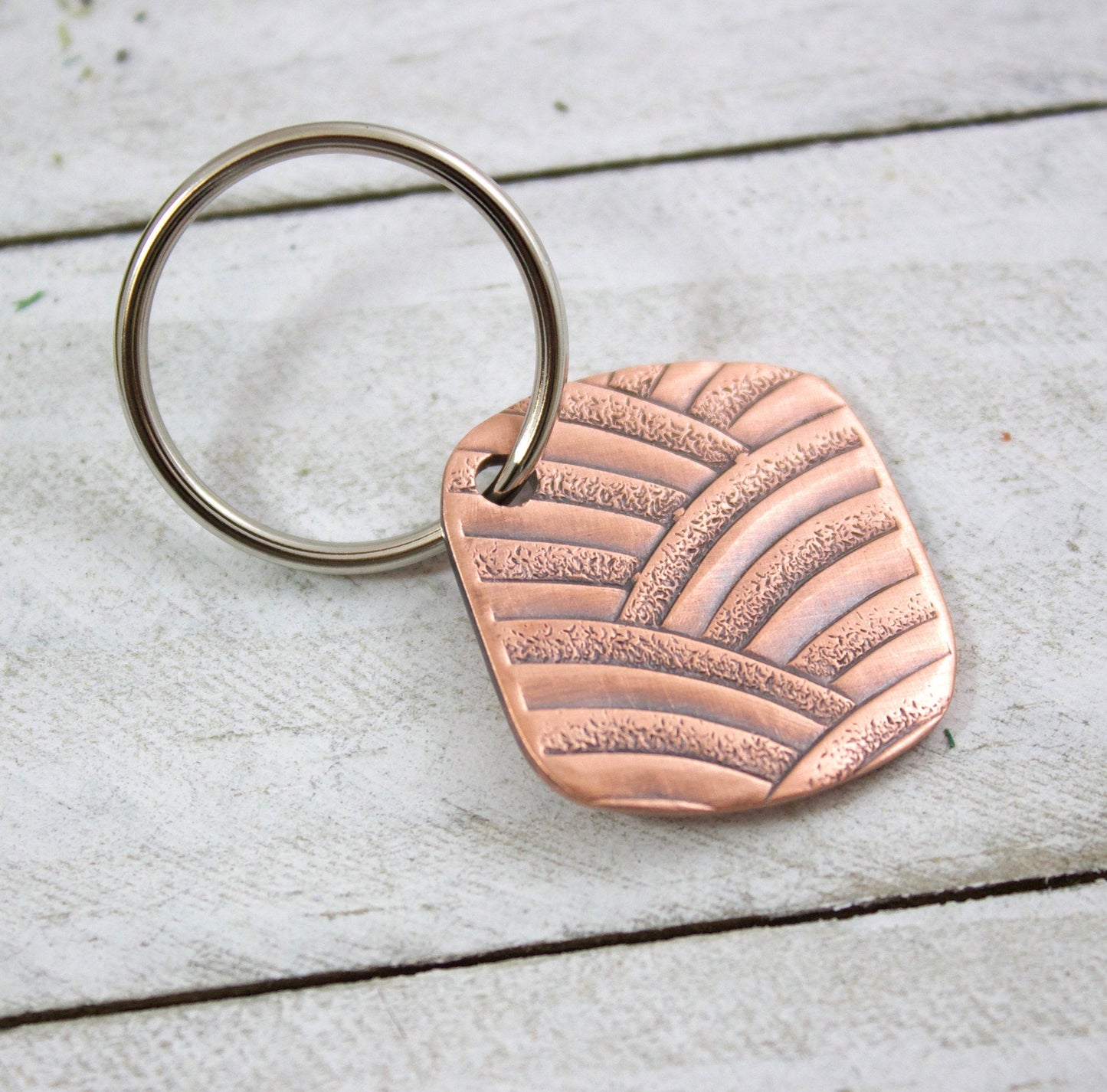 Copper keychain with a textured pattern of overlapping arches. Square with softly rounded corners.