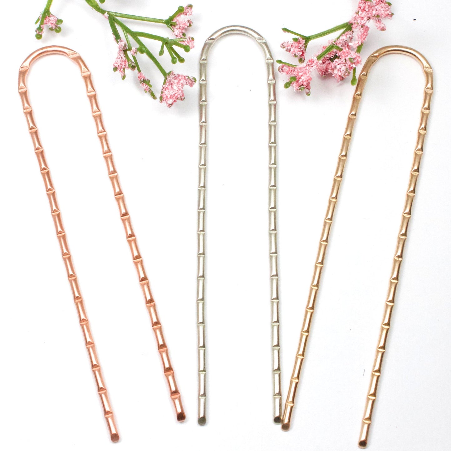 Copper, nickel, and bronze deep lines hair forks showing the actual size of a 5 inch hair fork. Stages with pink flowers.