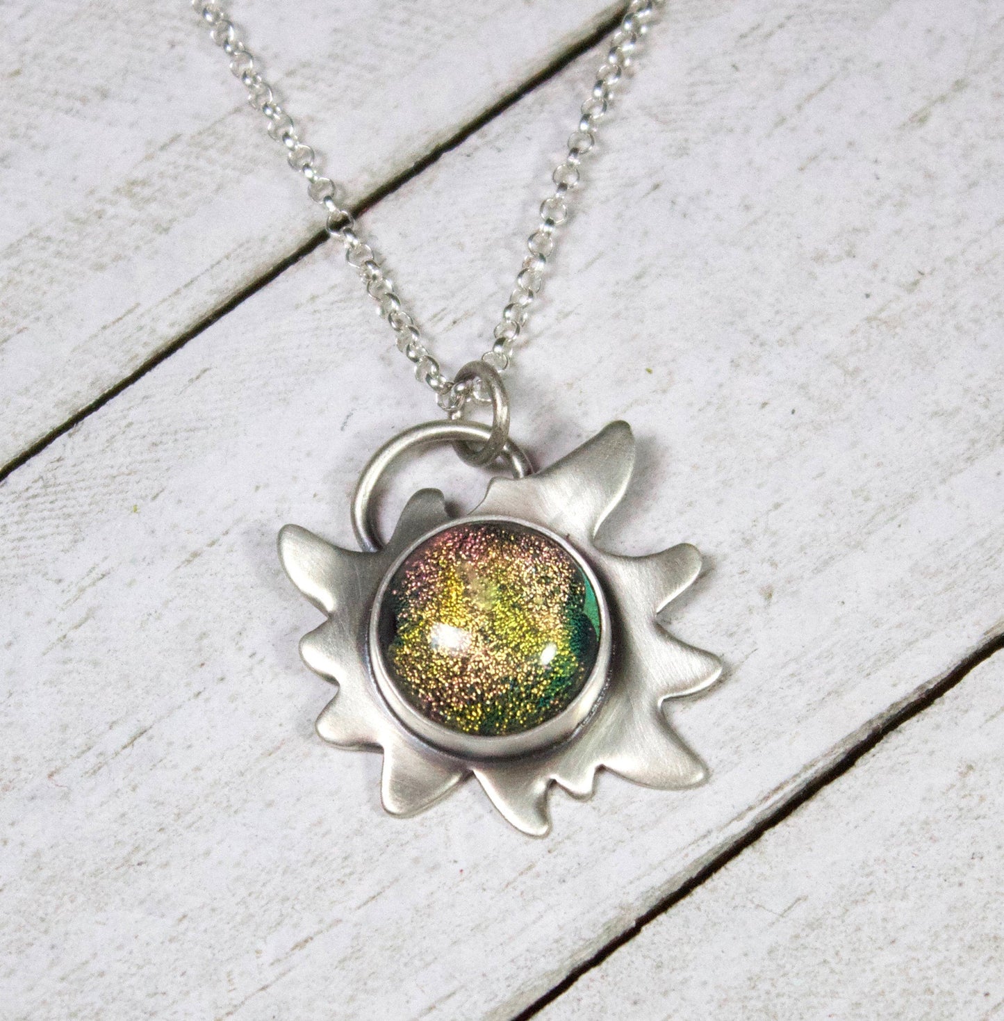 Edelweiss Flower Glass Stone Galaxy Pendant. This a one inch wide pendant made in sterling silver. The center is dichroic glass with sparkling bits in a golden color. The silver is shoped like an edelweiss flower. The sterling silver pendant comes on a rolo chain.