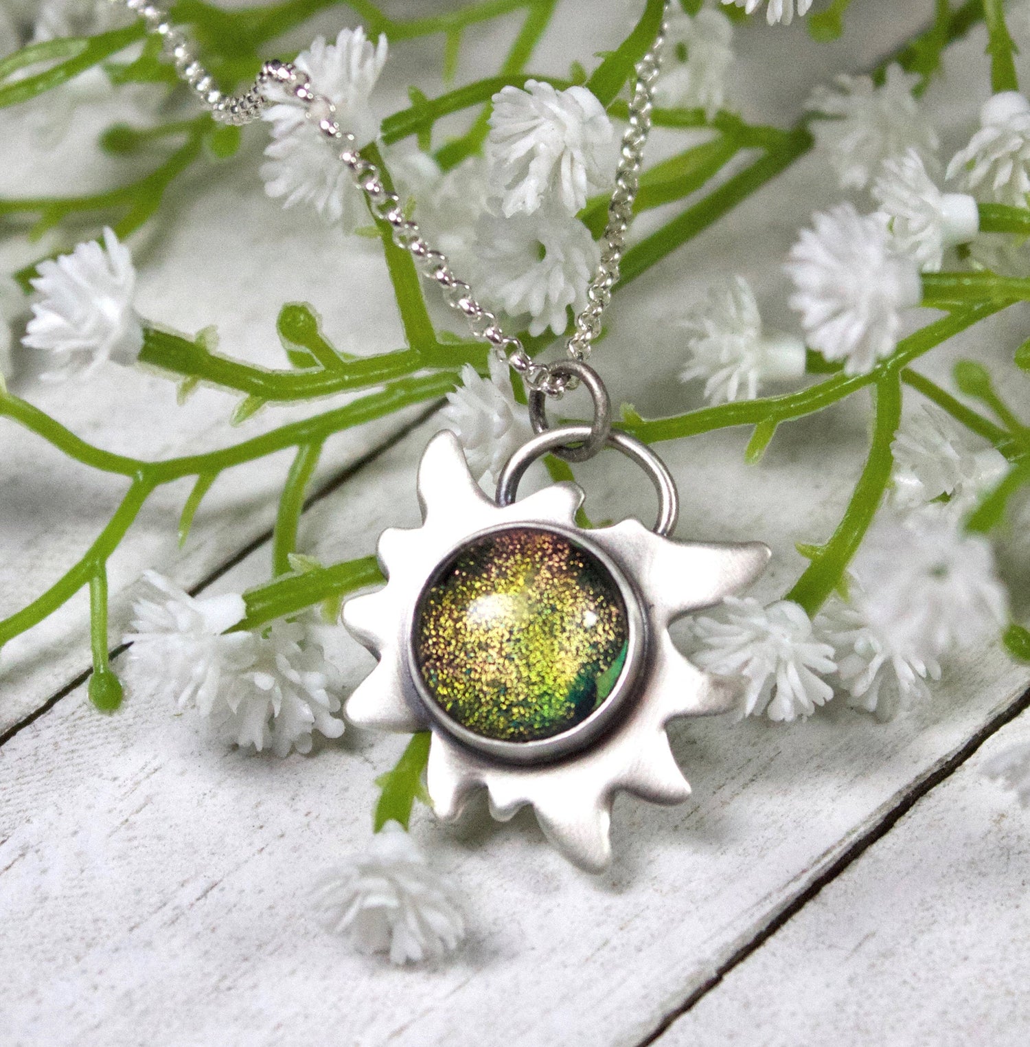 Edelweiss Flower Glass Stone Galaxy PendantEdelweiss Flower Glass Stone Galaxy Pendant. This a one inch wide pendant made in sterling silver. The center is dichroic glass with sparkling bits in a golden color. The silver is shoped like an edelweiss flower. The sterling silver pendant comes on a rolo chain.