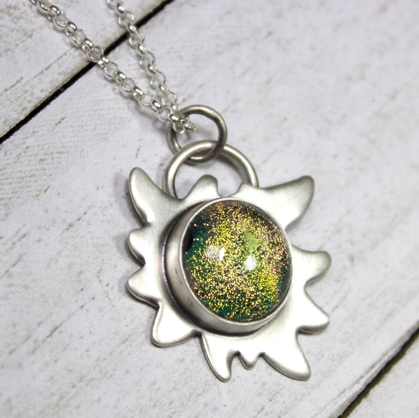 Edelweiss Flower Glass Stone Galaxy Pendant. This a one inch wide pendant made in sterling silver. The center is dichroic glass with sparkling bits in a golden color. The silver is shoped like an edelweiss flower. The sterling silver pendant comes on a rolo chain.