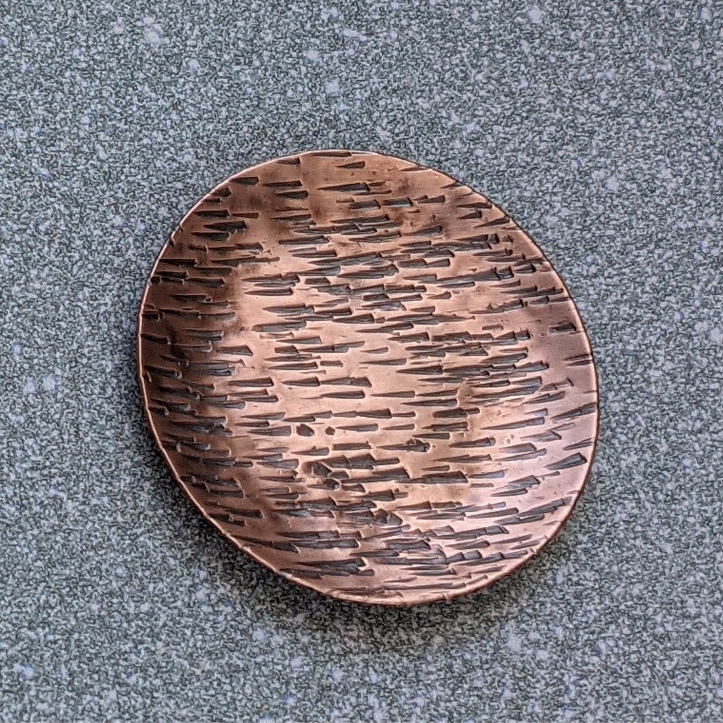 Small copper ring jewelry or trinket dish with a hammered texture resembling birch bark. The edges are curved up to form a shallow bowl.