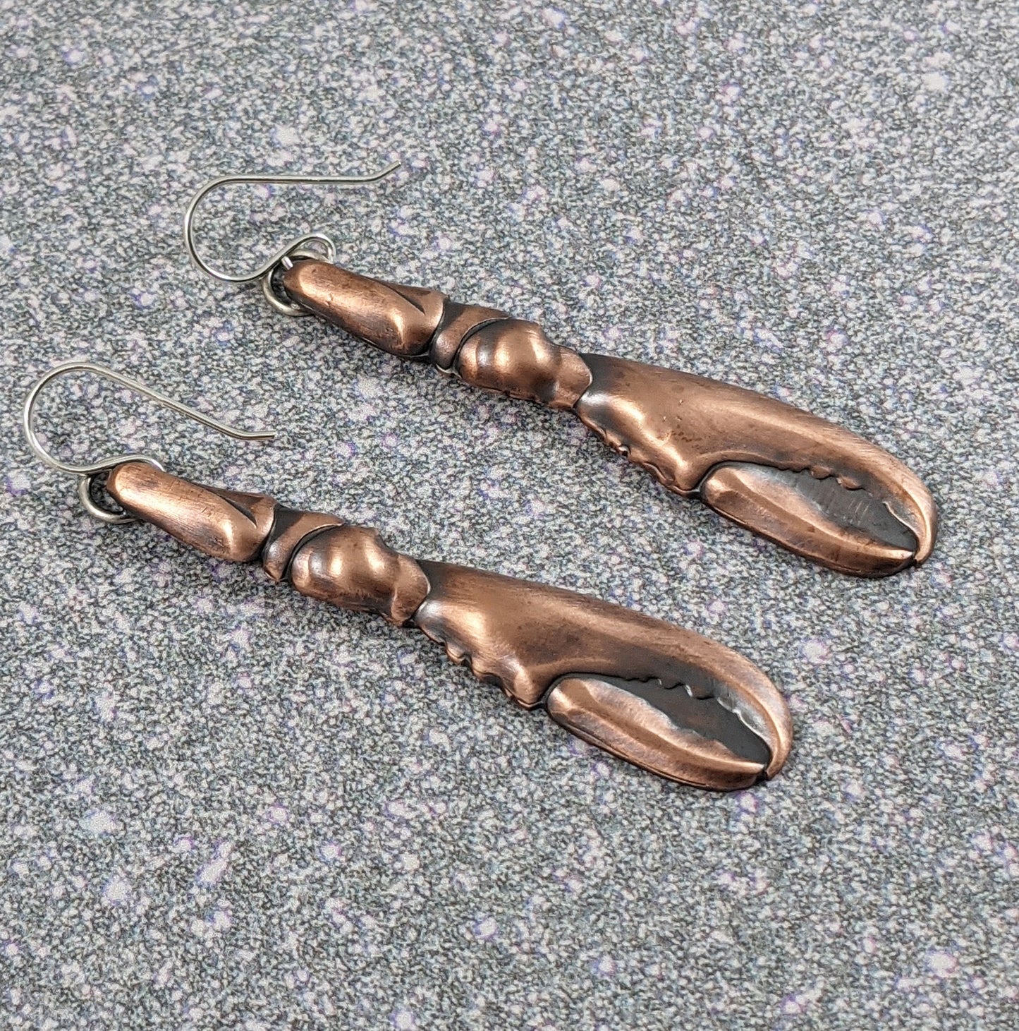 Copper earrings in the shape of a lobster claw. The claws are three dimensional and are on sterling silver ear wires. Posed on a gray background